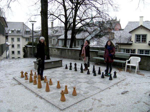 three students standing on a giant chess board
